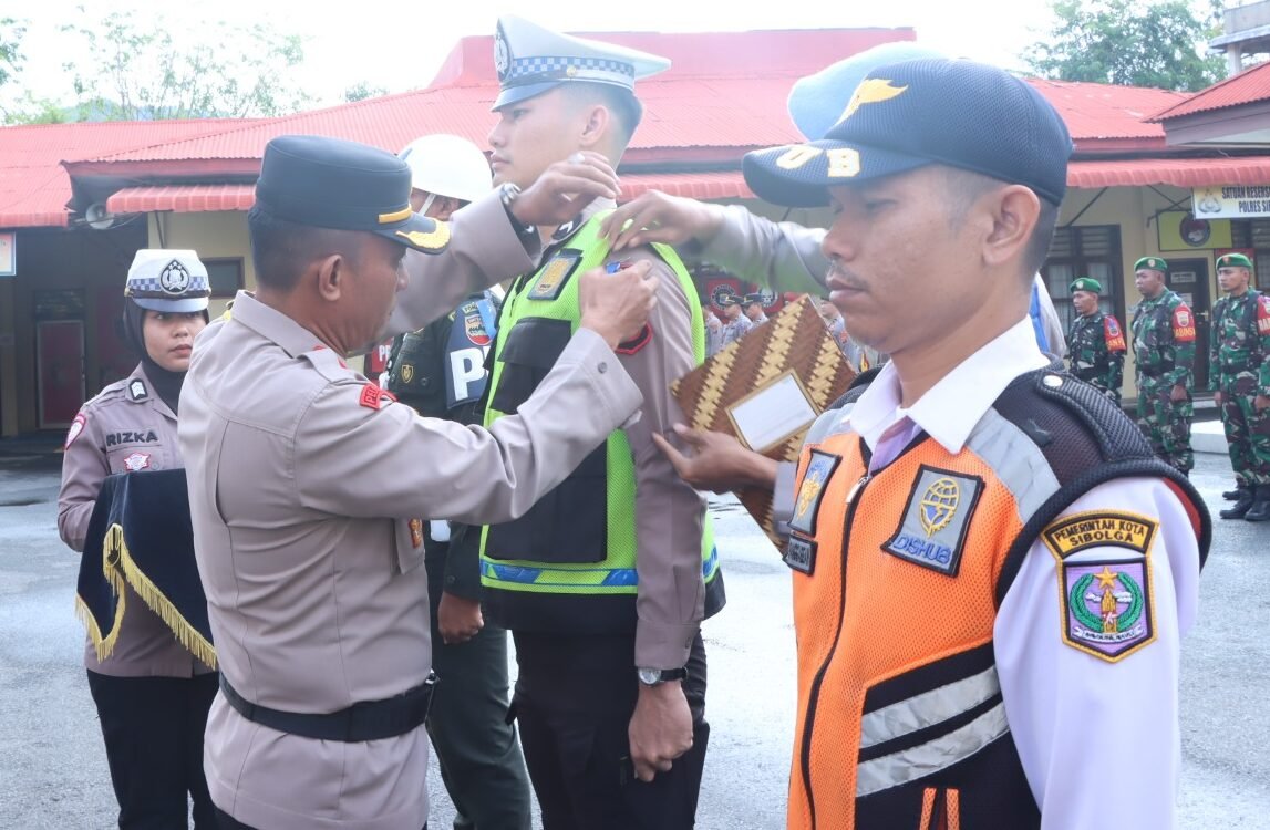 Wakapolres Sibolga Kompol Arifin B. Tampubolon saat menyematkan pita kepada personel sebagai tanda/ simbol dimulainya Ops Zebra Toba 2025 dilapangan Apel Polres Sibolga, Senin (17/11/2025)..