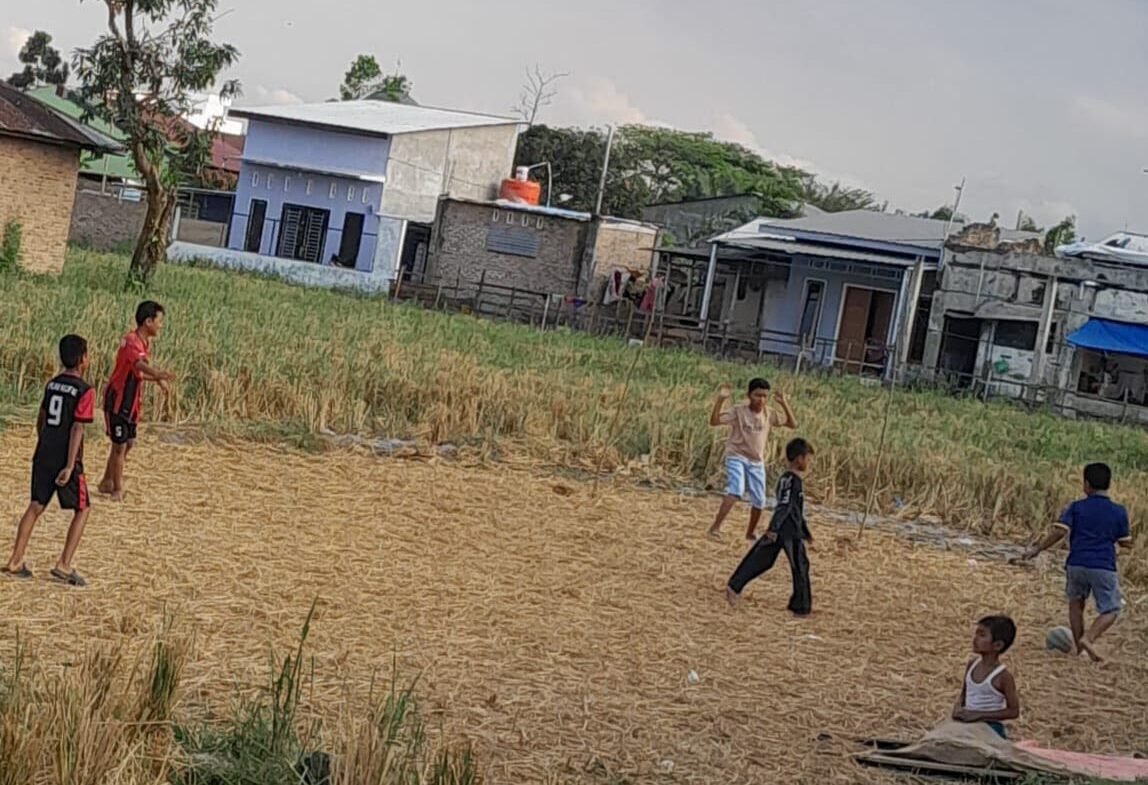 Para bocil bermain sepak bola di areal persawahan yang kering kerontang. 